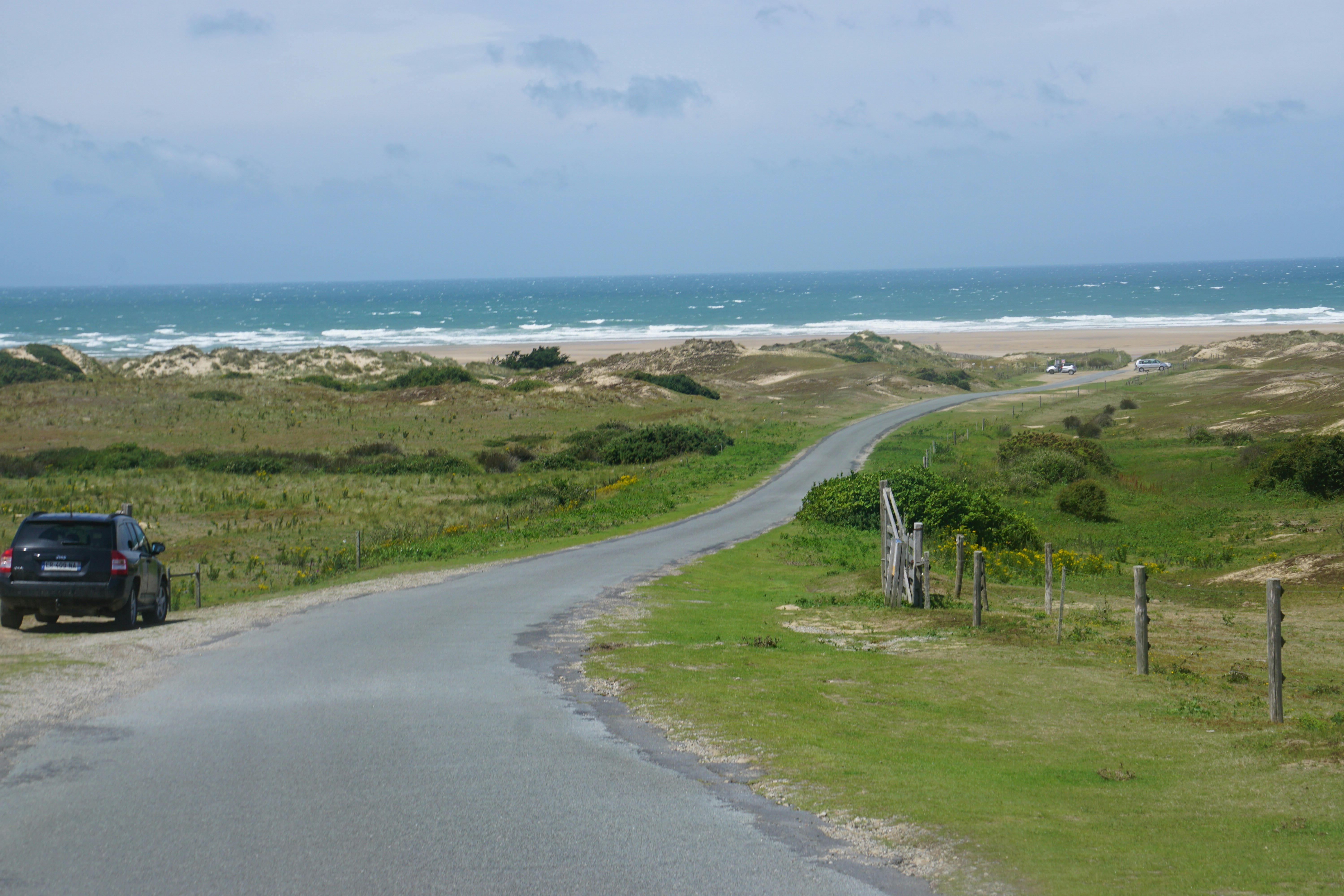 Narrow coastal road leading through sand dunes to a wide beach on the Atlantic coast of Cornwall