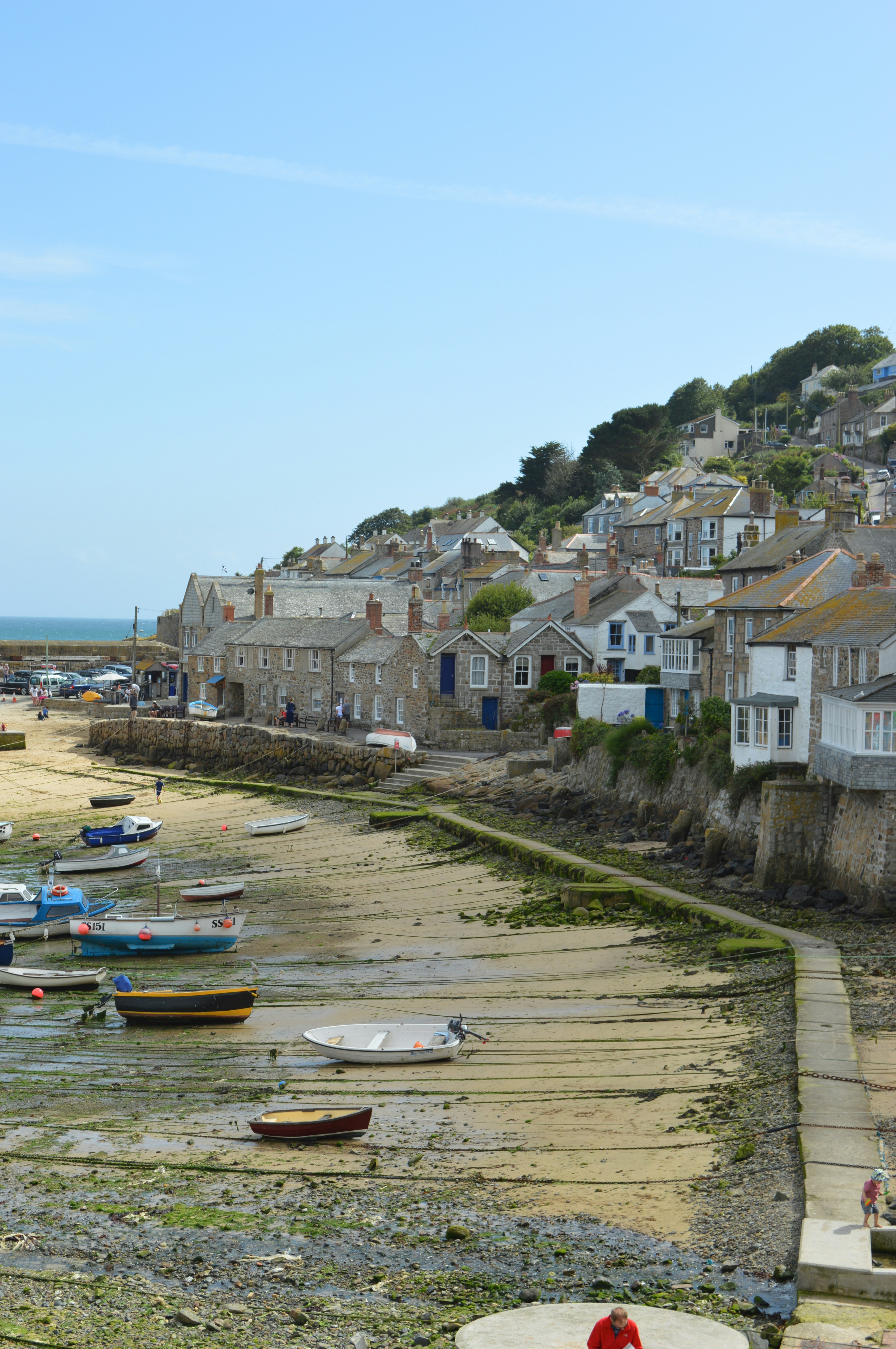 Small boats resting on the sand at low tide in Mousehole harbour with granite cottages along the waterfront