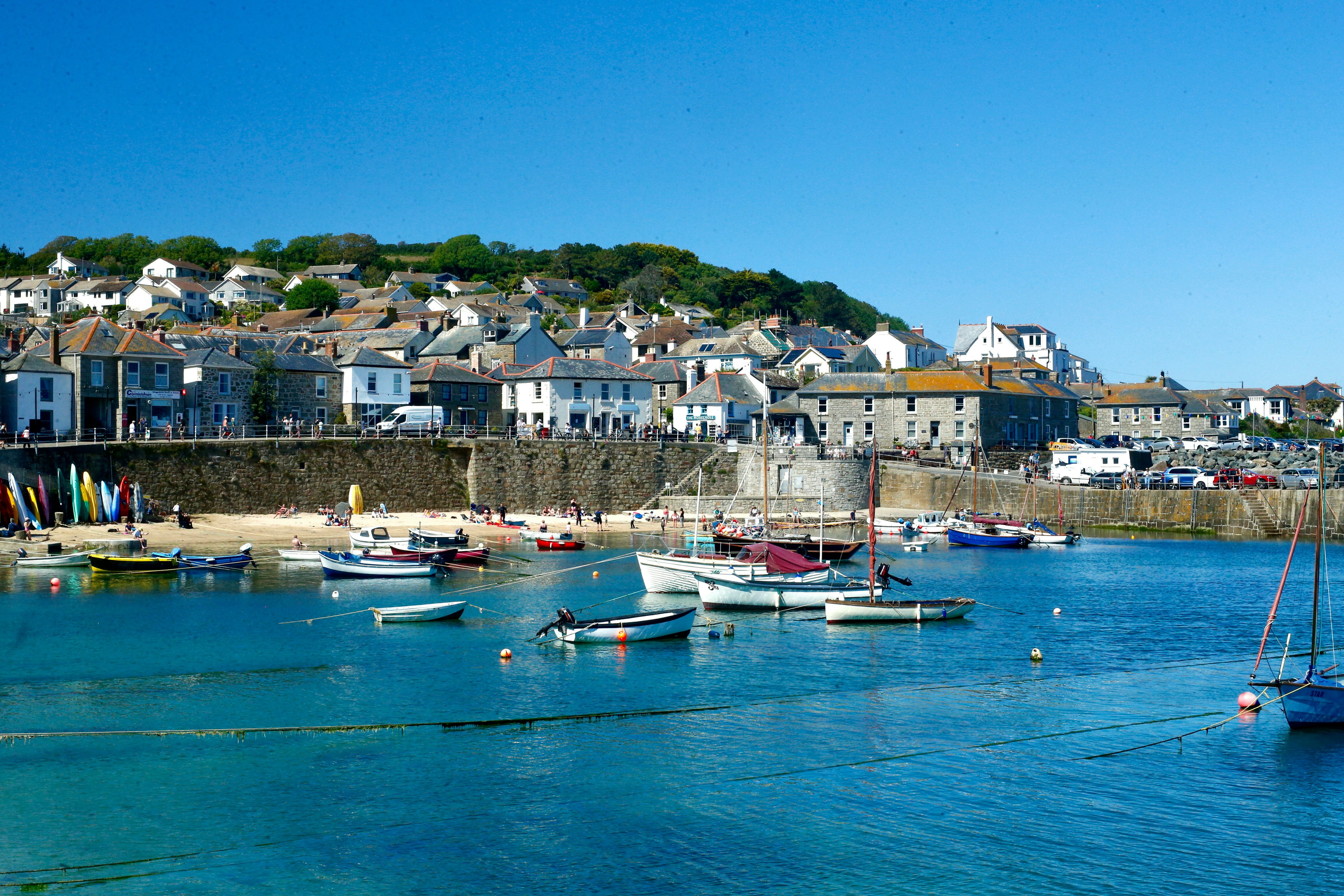 Boats afloat in St Ives harbour at high tide with the beach and cottages above the harbour wall