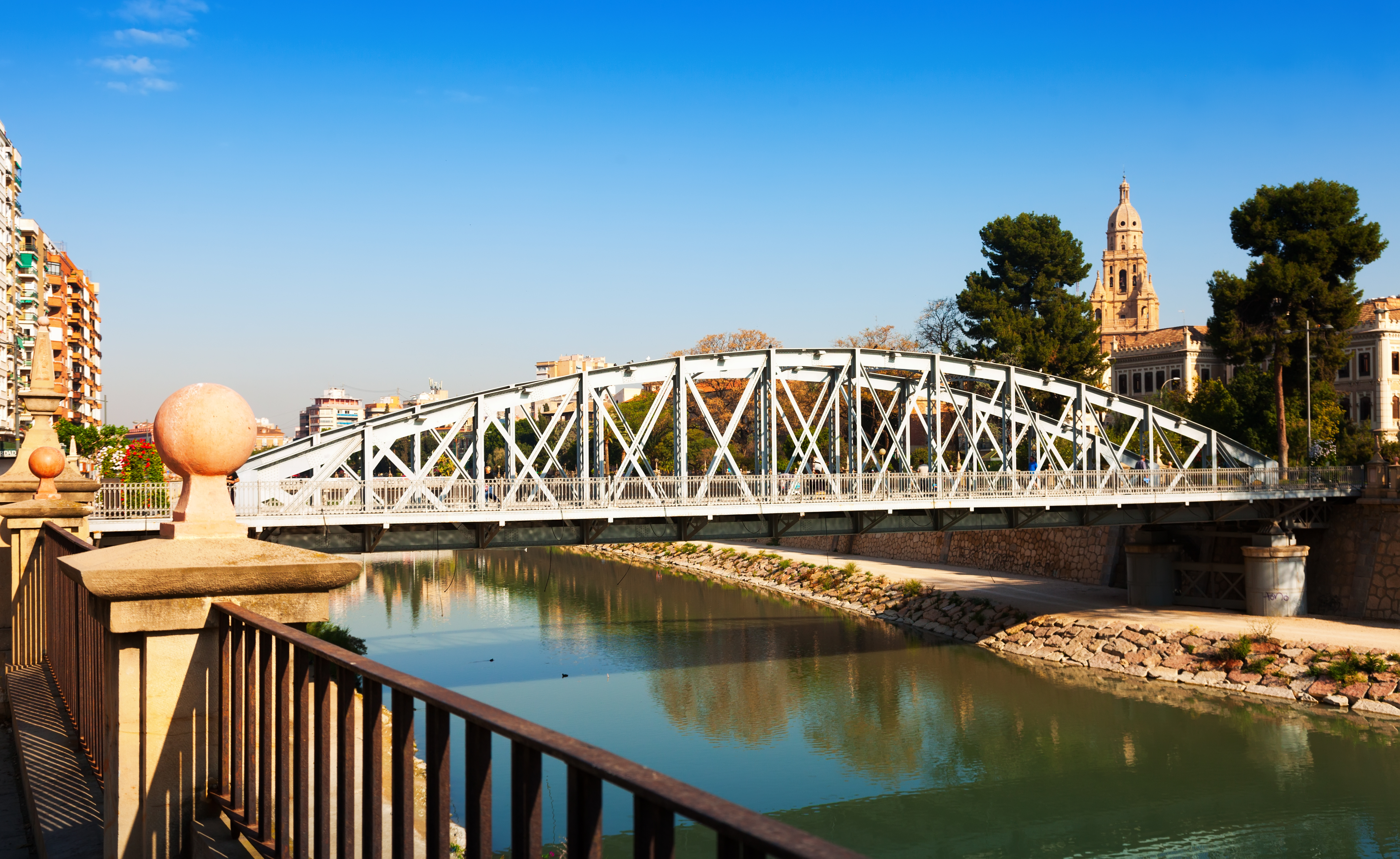Segura River in Murcia with pedestrian bridge and cathedral tower in the distance, near Floridablanca Gardens