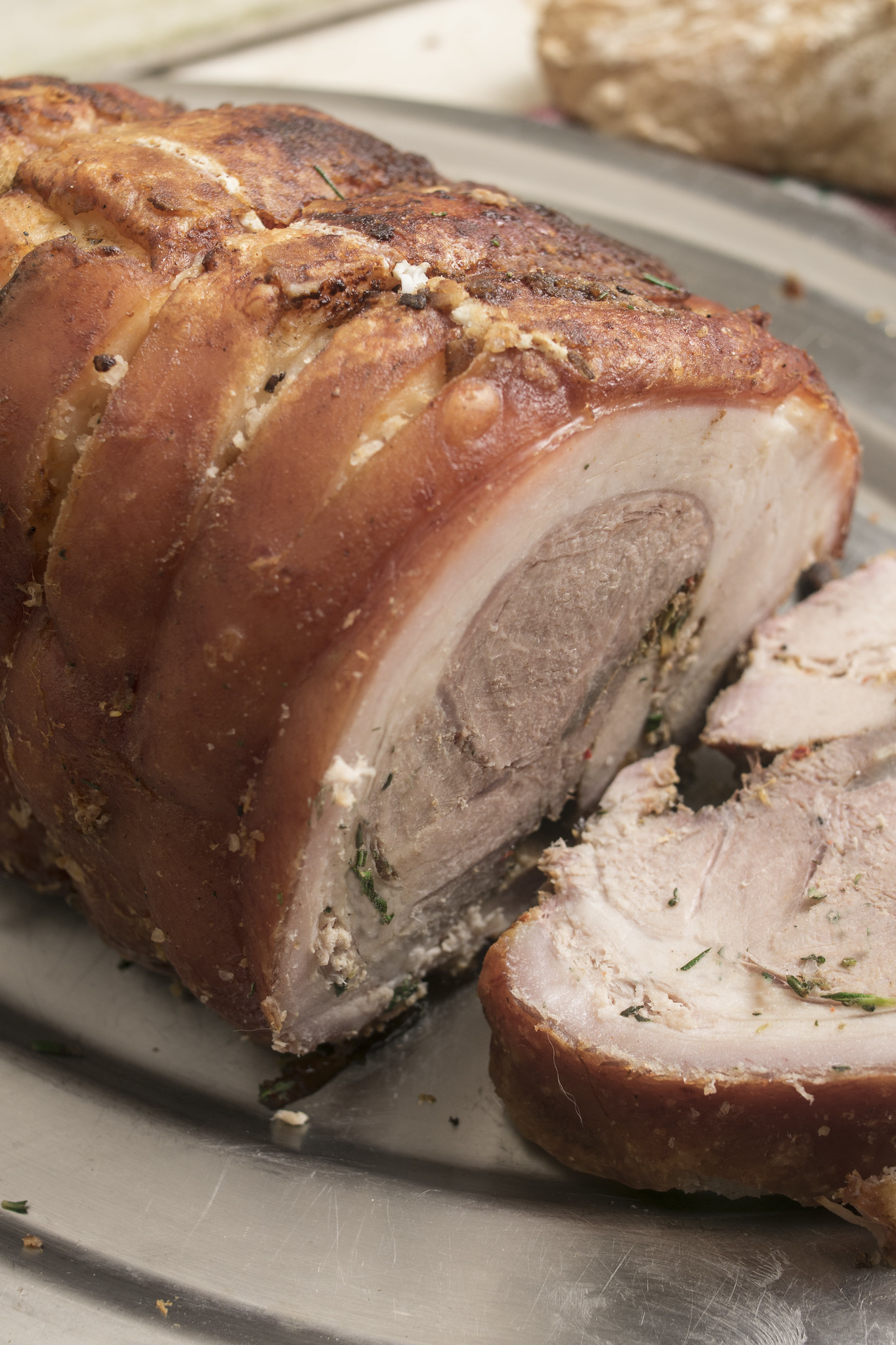 Sliced homemade porchetta showing the herby pork filling, crisp skin and rolled roast interior.