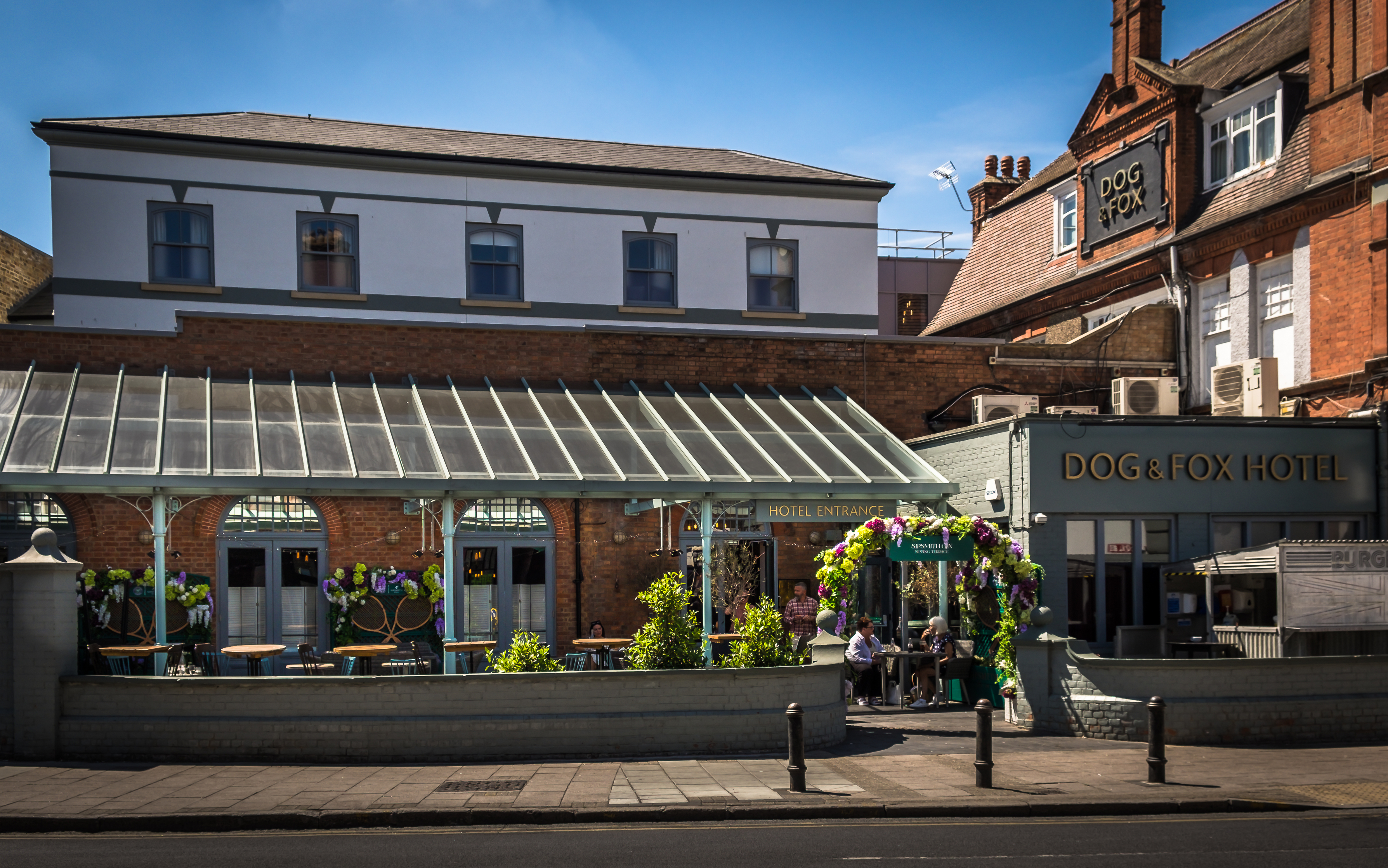 The Dog & Fox Hotel in Wimbledon Village, with outdoor seating and floral decorations on a sunny day.