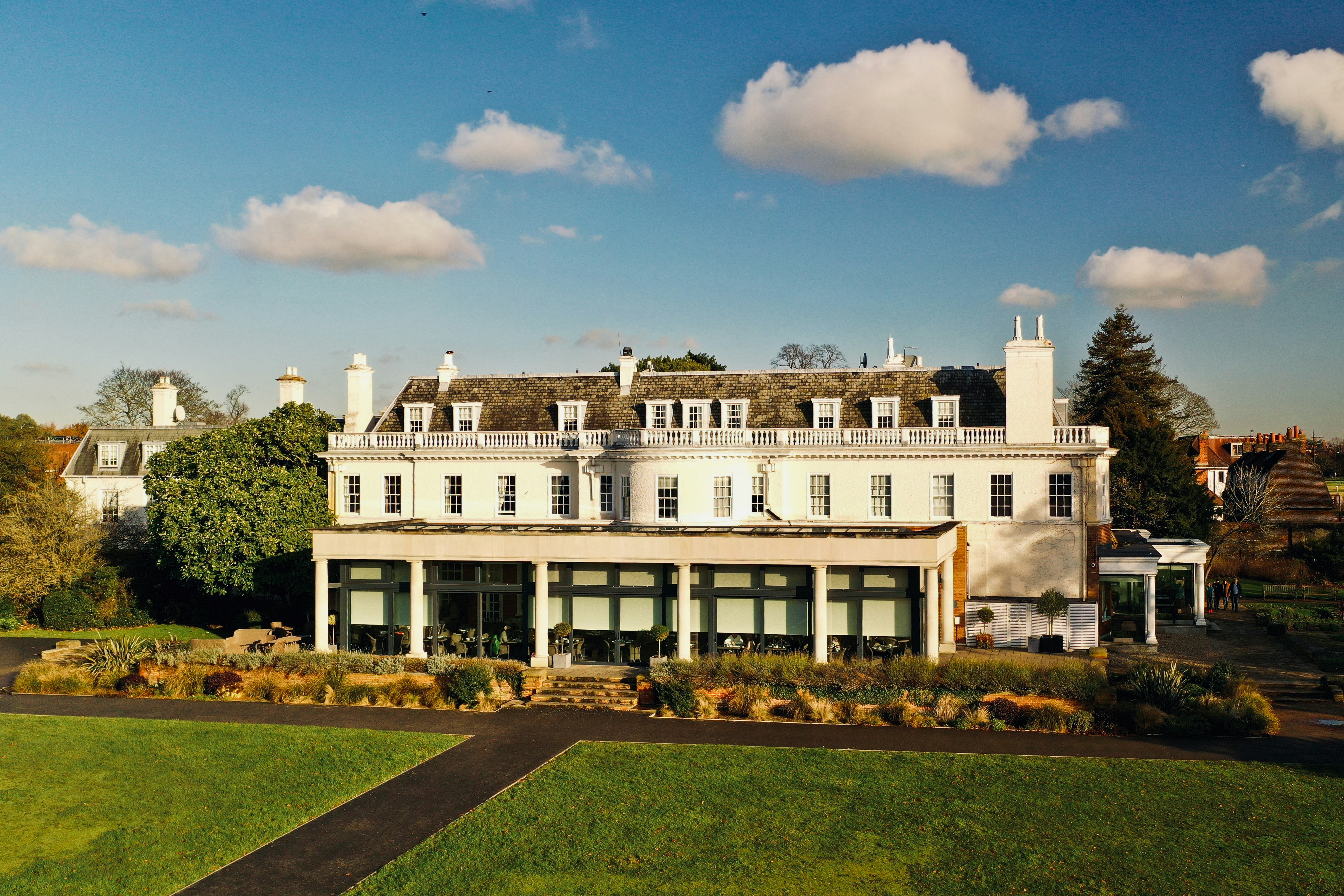 Hotel du Vin Cannizaro House in Wimbledon, a white Georgian-style hotel set beside green parkland under a blue sky.