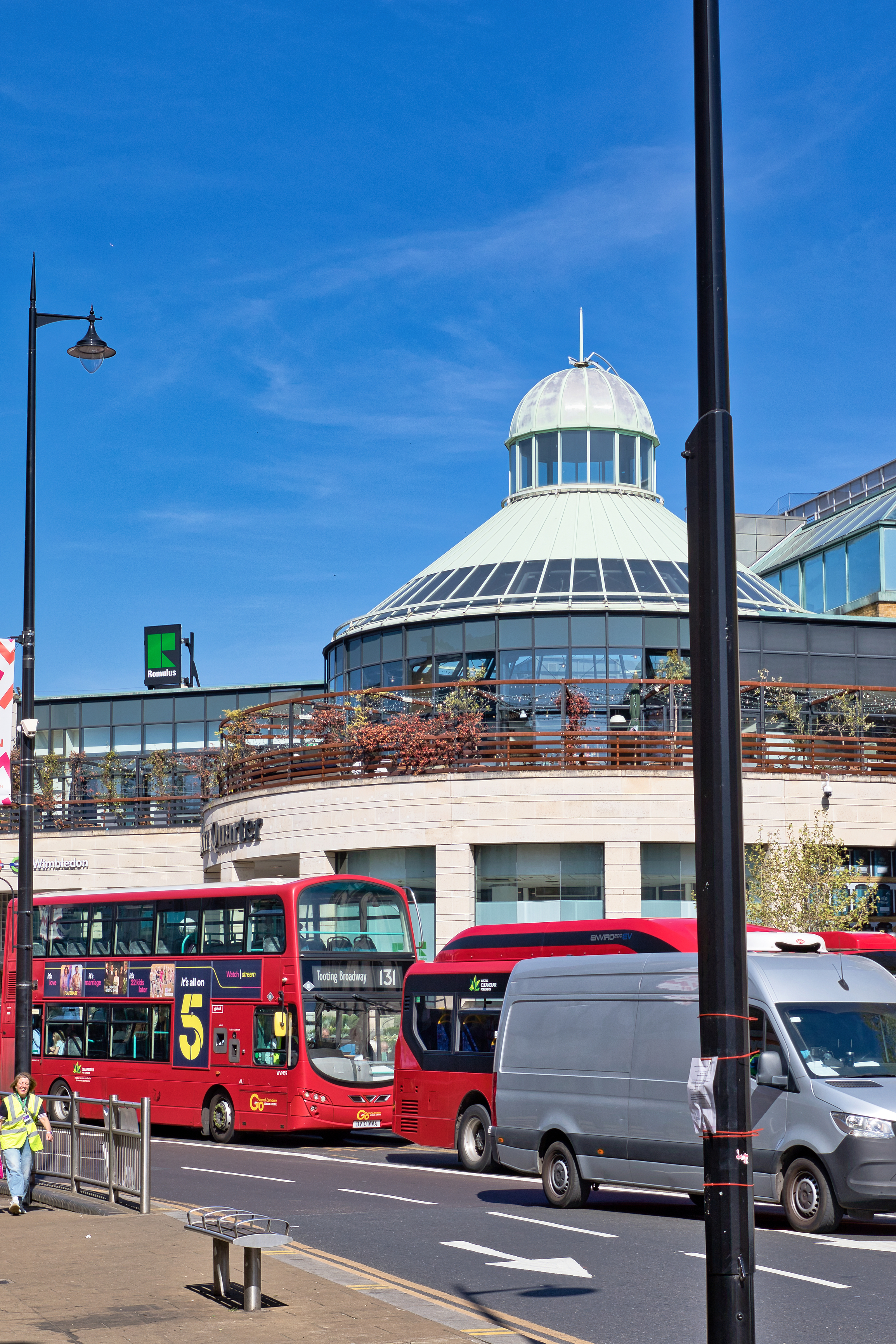 Red London buses pass through Wimbledon town centre near the station, showing the busy transport hub before the area opens out towards Wimbledon Village and the Common.
