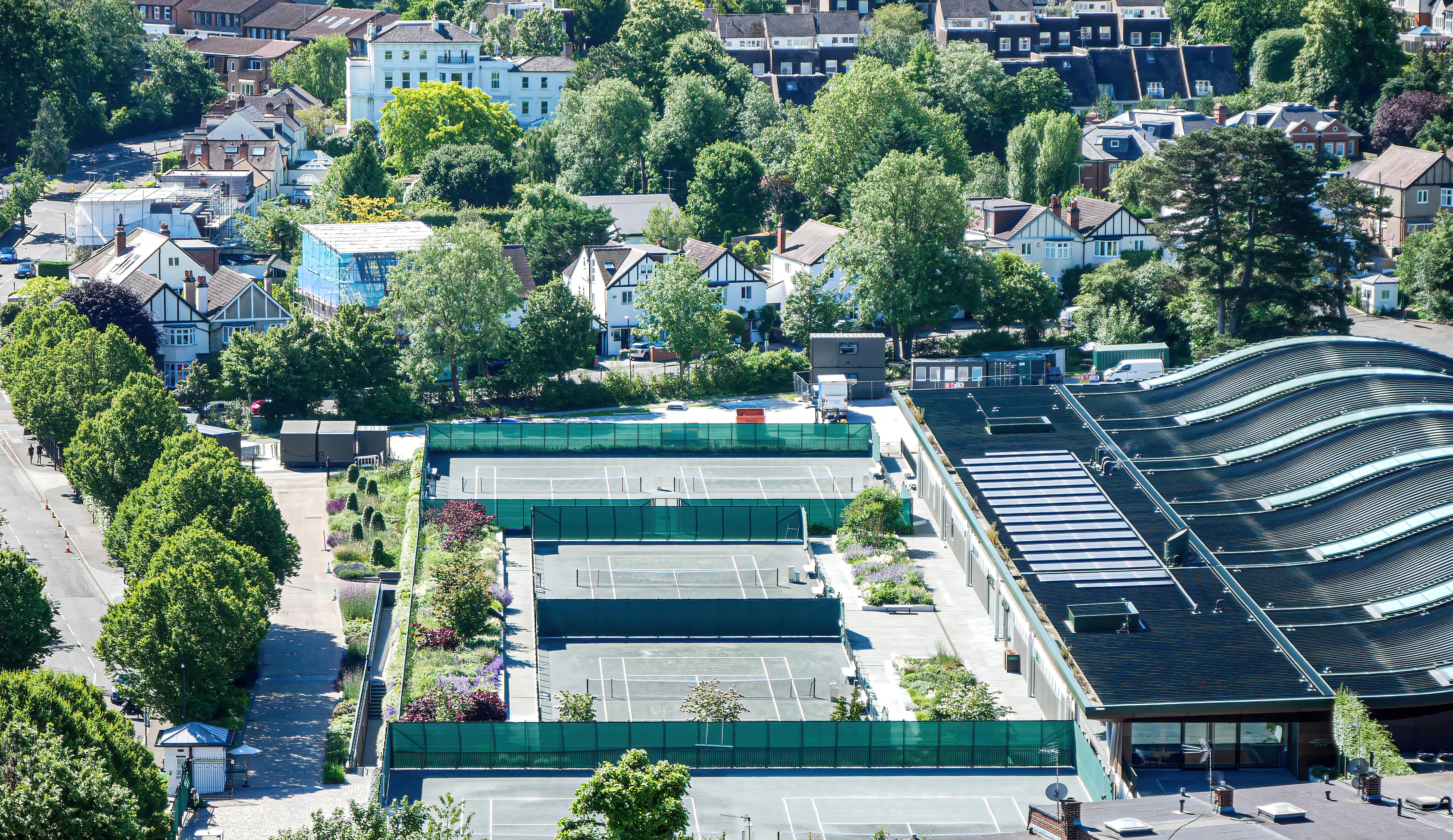 Aerial view of tennis courts surrounded by trees and houses in Wimbledon, London.