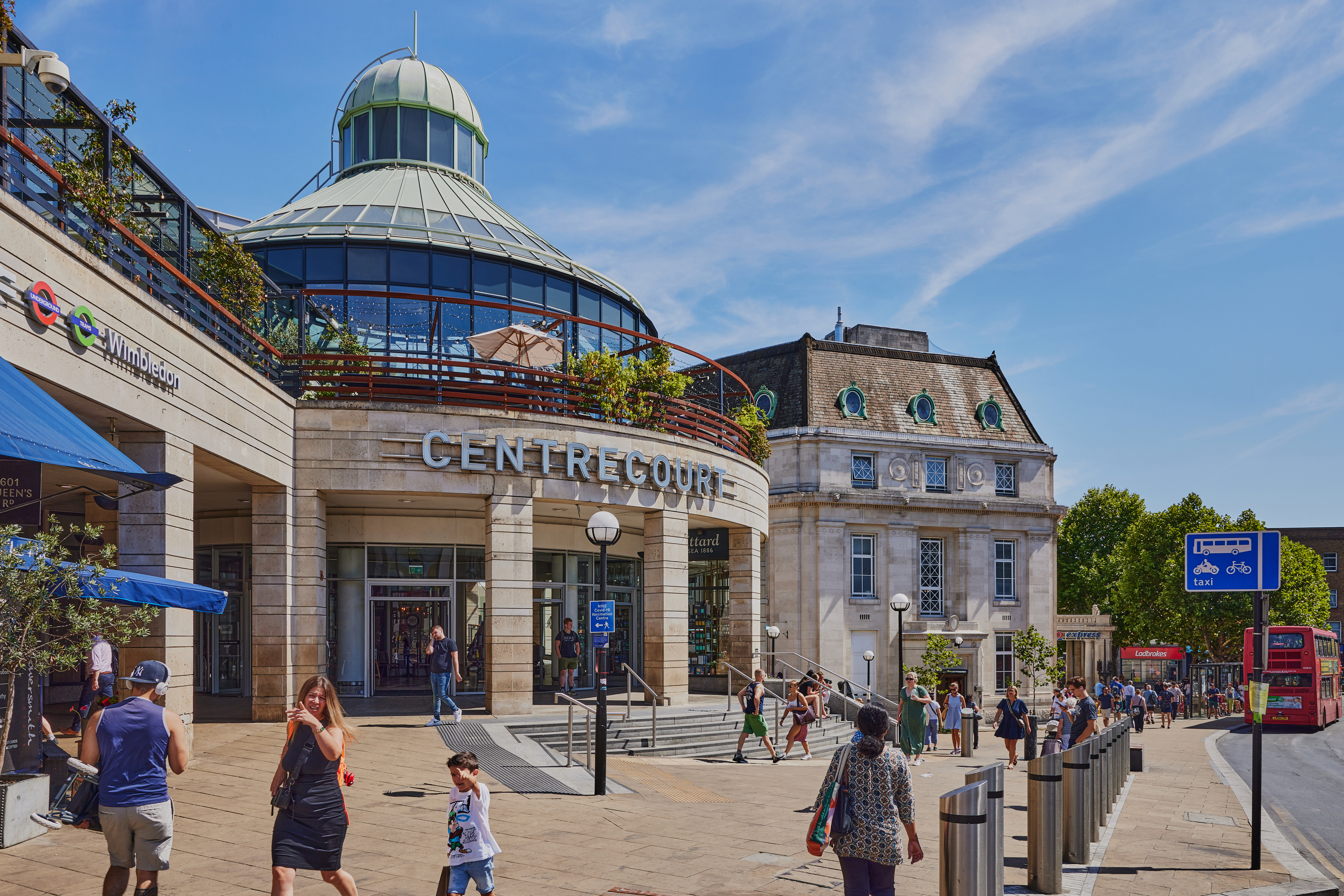 Wimbledon town centre with Centre Court shopping area, station signs, pedestrians and local transport links.